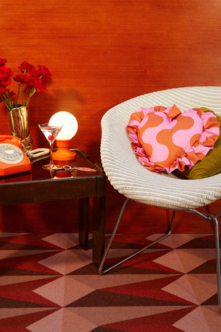 Retro kitsch interior styling with vintage Lloyd Loom chair, Weirdstock pink and orange retro heart ruffle cushion, vintage French lamp and orange telephone